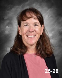 A smiling woman with brown hair, wearing a pink top and black cardigan, against a gray background.