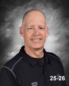A smiling man with short hair wearing a black polo shirt, set against a gray background, labeled "25-26."