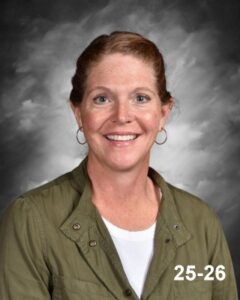 Smiling woman with red hair in a green jacket, set against a gray background.