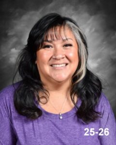Smiling woman with long, dark hair wearing a purple shirt, set against a gray background.
