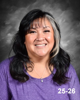 Smiling woman with long, dark hair wearing a purple shirt, set against a gray background.