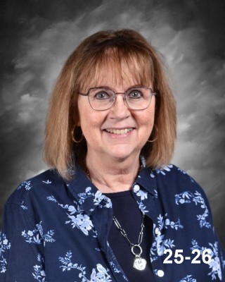 A smiling woman with shoulder-length brown hair, wearing glasses and a floral shirt, against a gray background.