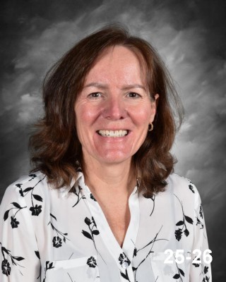 A smiling woman with shoulder-length brown hair wearing a floral blouse, set against a gray background.