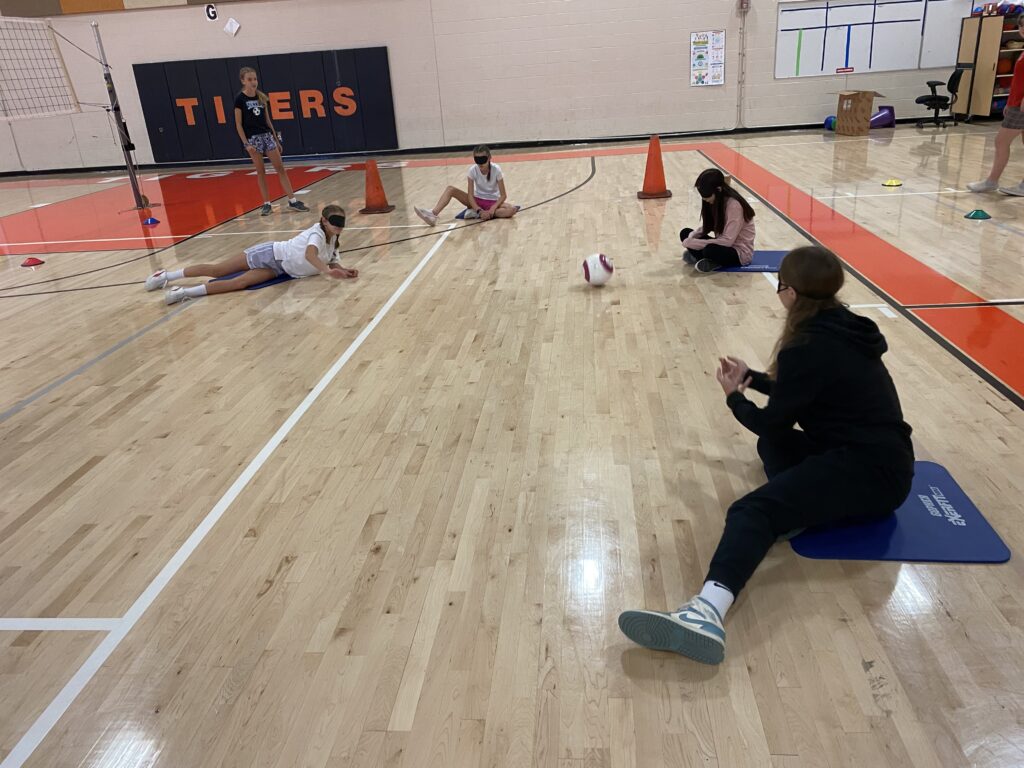 Foto de alumnos jugando un juego en el suelo del gimnasio con pliegues ciegos