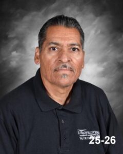 A man with short dark hair and a mustache is wearing a dark polo shirt, posing against a gray backdrop.