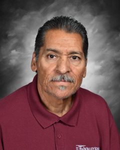 Man with short dark hair and a mustache wearing a maroon polo shirt with a gray, cloudy background.