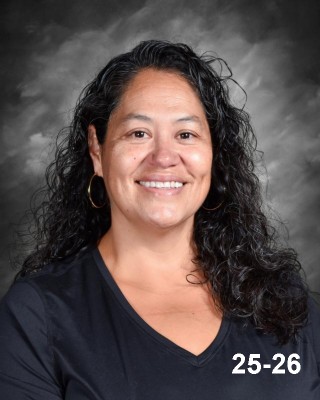 A smiling woman with long, curly hair wearing a black shirt, set against a gray background.