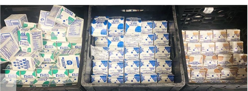 Three bins filled with various types of milk cartons, including whole, low-fat, and chocolate milk.