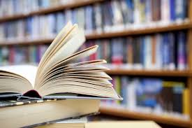 An open book in the foreground with a blurred background of bookshelves filled with books.